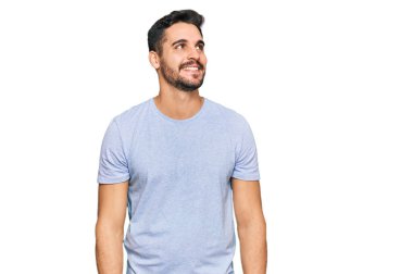 Gündelik kıyafetler giyen genç İspanyol bir adam yüzünde gülümsemeyle yan yana bakıyor, doğal bir ifade. Kendinden emin gülen. 