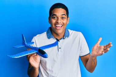 Genç yakışıklı İspanyol adam uçak oyuncağı tutuyor başarıyı mutlu bir gülümsemeyle kutluyor ve kazanan el kaldırarak ifade ediyor 