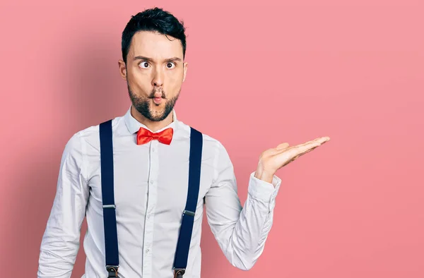 Hispanic man with beard presenting with open palm making fish face with mouth and squinting eyes, crazy and comical.