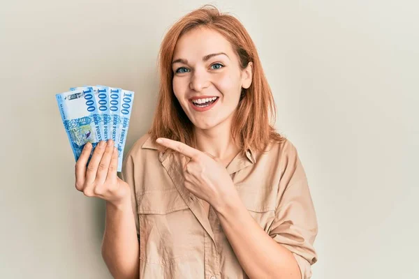Young caucasian woman holding hungarian forint banknotes smiling happy pointing with hand and finger