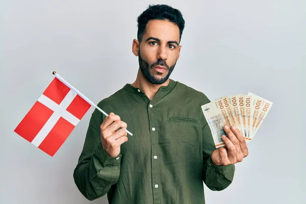 Młody Hiszpan Trzymający Flagę Denmarkową Banknoty Koronowe Robiący Rybią Twarz — Zdjęcie stockowe