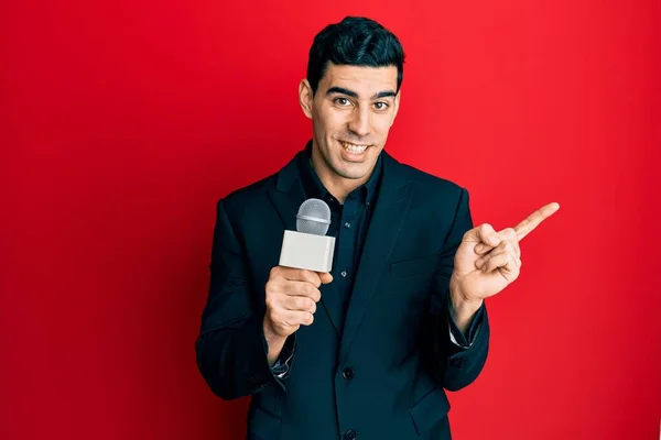 Hezký Hispánský Muž Držící Reportérský Mikrofon Šťastně Usmívá Ukazuje Rukou — Stock fotografie