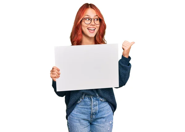 Jovem Ruiva Segurando Banner Vazio Apontando Polegar Para Lado Sorrindo — Fotografia de Stock