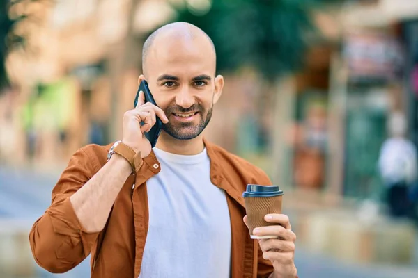 Young hispanic bald man talking on the smartphone drinking coffee at the city.