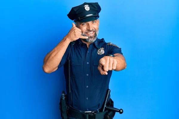 Middle age handsome man wearing police uniform smiling doing talking on the telephone gesture and pointing to you. call me.
