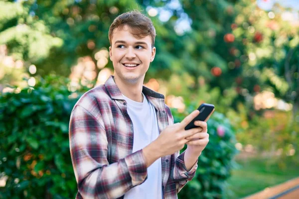 公園でスマホを使って幸せそうに笑う若い白人男性 — ストック写真