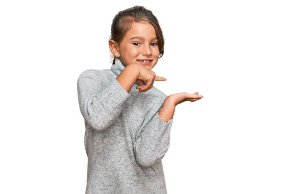 手で提示しながら 指で指差しながらカジュアルなタートルネックセーターを身に着けている小さな美しい女の子は驚きとカメラに笑顔 — ストック写真