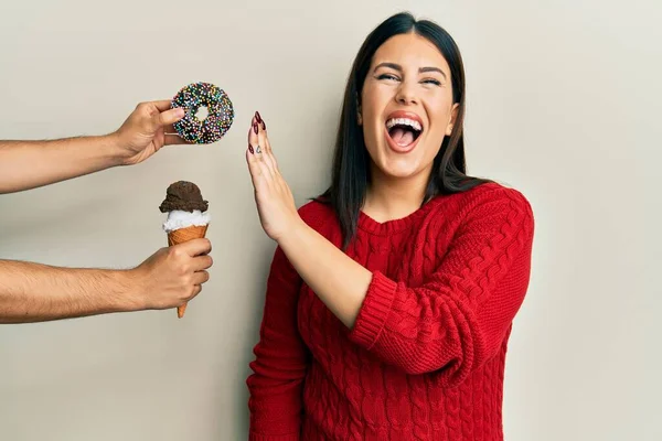 Beautiful brunette woman saying no to sweets on a healthy diet smiling and laughing hard out loud because funny crazy joke.