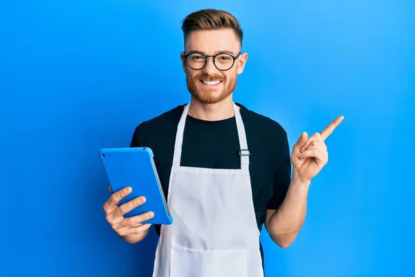 Jovem Ruiva Vestindo Avental Profissional Usando Touchpad Sorrindo Feliz Apontando — Fotografia de Stock