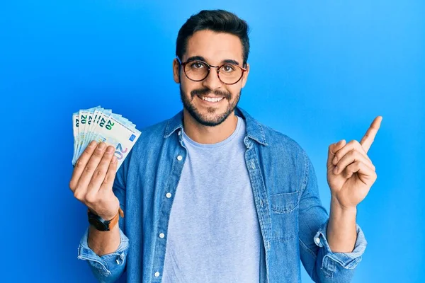 Joven Hispano Sosteniendo Montón Billetes Euros Sonriendo Feliz Señalando Con — Foto de Stock