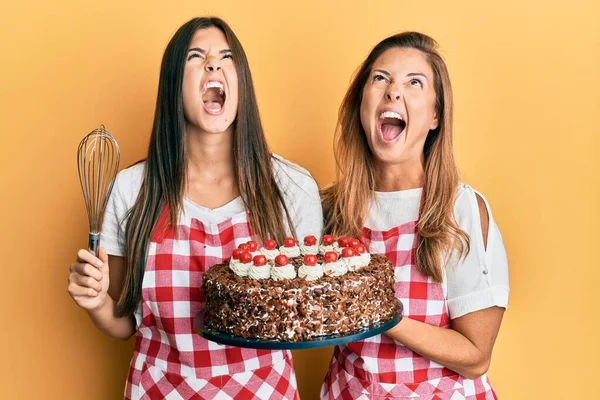母親と娘のヒスパニック系の家族を身に着けているパン屋エプロンを保持自家製ケーキ怒っていると怒っている叫び不満と激怒 怒りで叫んで検索 — ストック写真