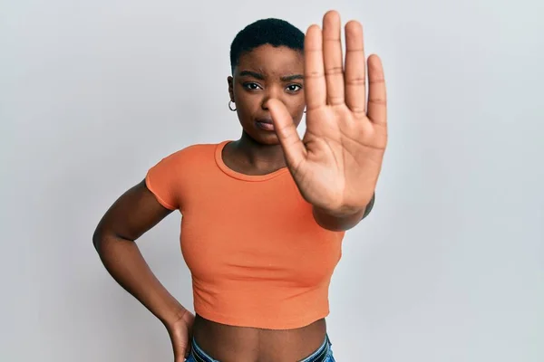 カジュアルなオレンジのTシャツを着た若いアフリカ系アメリカ人女性が手の手のひらで歌うのをやめます 顔に負の重大なジェスチャーで — ストック写真