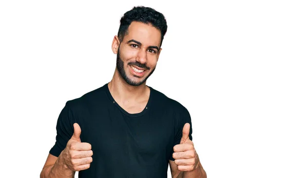 髭を生やしたヒスパニック系の男性は 手で積極的なジェスチャーを行うカジュアルな黒のTシャツの成功のサインを着て 親指を笑顔と幸せ 陽気な表情と勝者のジェスチャー — ストック写真