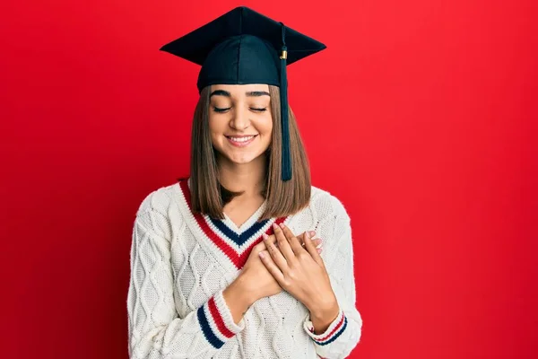 目を閉じて胸の上で手で笑顔卒業キャップを身に着けている若いブルネットの女の子と顔に感謝のジェスチャー 健康の概念 — ストック写真