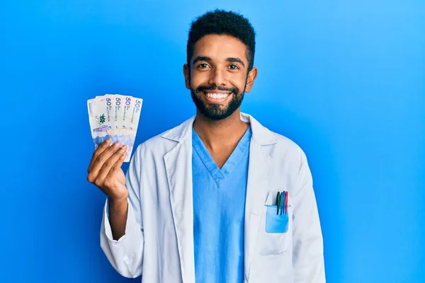 Przystojny Latynos Brodą Mundurze Lekarza Trzymający Kolumbijskich Pesos Wyglądających Pozytywnie — Zdjęcie stockowe