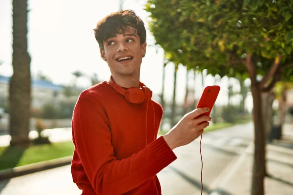 Young hispanic man smiling happy using smartphone and headphones at the city.