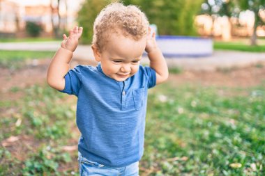 Sevimli ve mutlu küçük çocuk güneşli bir günde parkta eğleniyor. Güzel sarı saçlı erkek çocuk dışarıda oynuyor.