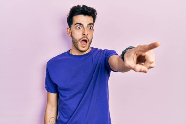 Gündelik tişört giyen genç İspanyol erkeği parmağıyla işaret ediyor. İleriyi işaret ediyor, ağzı açık, şaşkın, ön tarafta bir şey var. 