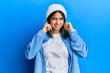 Gürültülü müzik sesi için sevimli yün şapkalı, parmaklarıyla kulaklarını kapatan genç Latin bir kadın. sağır kavramı. 