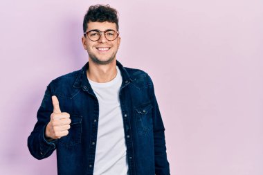 Gündelik giysiler ve gözlük takan İspanyol genç adam elleriyle mutlu bir jest yapıyor. Kameraya bakıp başarıyı gösteren ifade. 