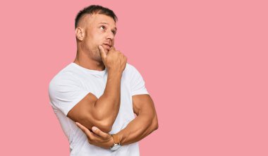 Yakışıklı, beyaz tişört giyen, bir soru hakkında endişelenen, eli çenesinde endişeli ve gergin bir adam. 