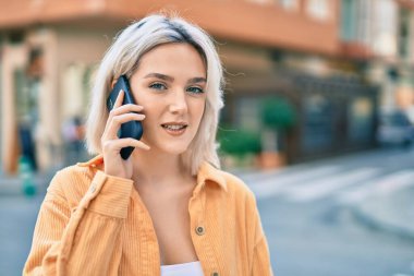 Genç sarışın kız gülümsüyor. Şehirdeki akıllı telefondan konuşuyor..