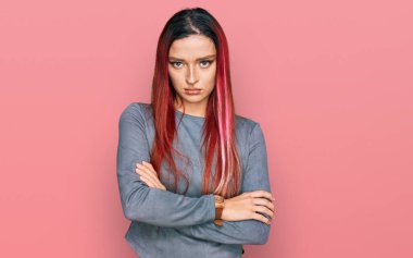 Gündelik kıyafetler giyen, kuşkucu ve gergin genç beyaz bir kadın. Yüzünde çapraz kollarla onaylamayan bir ifade var. negatif kişi. 