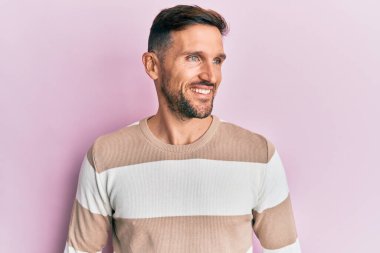 Sakallı, sıradan kıyafetler giyen, rahat bir görünüm takınan, kendine güvenen ve gülümseyen yakışıklı bir adam.. 