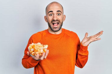 Patates cipsi tutan genç kel adam başarıyı mutlu bir gülümsemeyle ve kazanan yüz ifadesiyle kutluyor. 