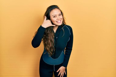 Genç İspanyol kız neoprene üniforması giyip gülümsüyor telefonla el ve parmak hareketleri yapıyor telefonda konuşuyor gibi. iletişim kavramları. 