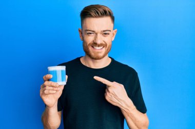 Kulak kiri temizleyici tutan genç kızıl saçlı adam gülümsüyor. 