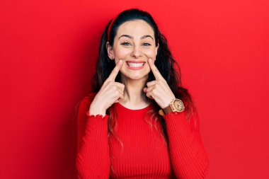 Gündelik kıyafetler giyen, ağzı açık gülümseyen, parmakları işaret eden ve neşeli gülümsemeye zorlayan genç İspanyol kadın. 