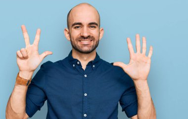 Gündelik kıyafetler giyen genç İspanyol adam sekiz numarayı gösterip işaret ederken kendinden emin ve mutlu bir şekilde gülümsüyor.. 