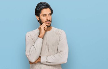 Gündelik kıyafetler giyen genç İspanyol bir adam ciddi bir yüz ifadesi, eli çenesinde soru soran, kafa karıştırıcı bir fikir hakkında düşünceli. 