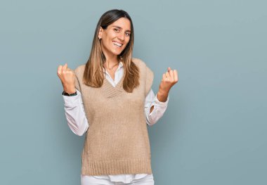 Gündelik kıyafetler giyen genç bir kadın çok mutlu ve heyecanlı. Kazanan bir jest yapıyor. Kolları havada, gülümsüyor ve başarı için bağırıyor. kutlama konsepti. 