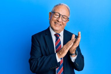 Beyaz üst düzey bir adam iş elbisesi ve kravat takıyor mutlu ve neşeli alkışlıyor, gururla gülümsüyor. 