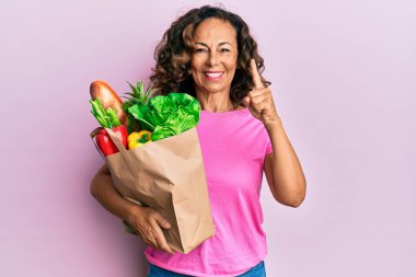 Orta yaşlı İspanyol kadın elinde ekmek ve bakkaliyeyle bir kese kağıdıyla bir fikir ya da soru işareti ile gülümsüyor. 