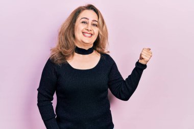 Orta yaşlı beyaz kadın, günlük kıyafetler giyiyor, gülümsüyor, gülümsüyor ve başparmağıyla yan tarafı işaret ediyor.. 