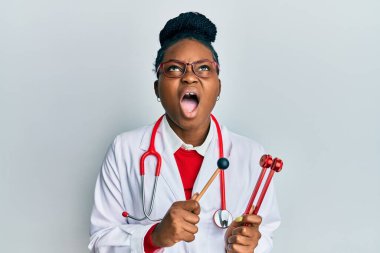 Genç Afrikalı Amerikalı kadın doktor üniforması giyiyor çatalı ayarlıyor kızgın ve kızgın çığlık atıyor sinirli ve öfkeli, öfkeyle bağırıyor.. 