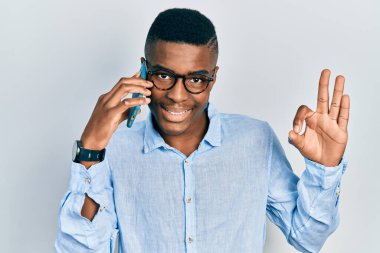Genç Afro-Amerikalı adam akıllı telefondan konuşuyor parmaklarıyla imza atıyor, gülümsüyor ve mükemmel bir sembol oluşturuyor. 