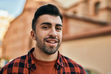 Genç İspanyol adam gülümseyerek şehirde mutlu mesut dikiliyor..