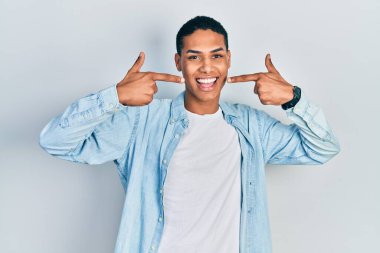 Gündelik kıyafetler giyen, neşeli gülümseyen, parmaklarıyla ve ağzıyla işaret eden Afro-Amerikan genç adam. diş sağlığı kavramı. 