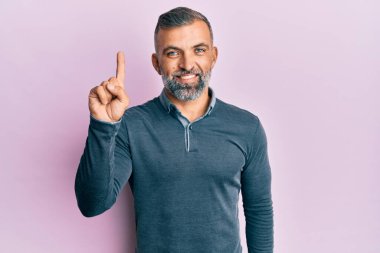 Orta yaşlı, sıradan kıyafetler giyen yakışıklı bir numaralı parmağını gösterip onu gösterirken kendinden emin ve mutlu bir şekilde gülümsüyor.. 