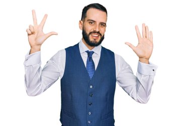 Sakallı genç adam iş yeleği giyiyor ve 8 numaralı parmaklarını gösterip gülümsüyor. Kendinden emin ve mutlu.. 