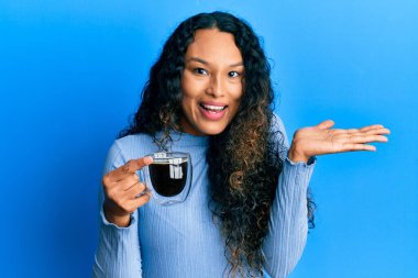 Genç Latin kadın kahveyle zaferi kutluyor mutlu bir gülümsemeyle ve kazanan el kaldırarak. 