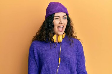 Kıvırcık saçlı, müzik dinleyen, kulaklık takan, kameraya seksi bir ifadeyle bakan, neşeli ve mutlu yüzlü genç esmer kadın.. 