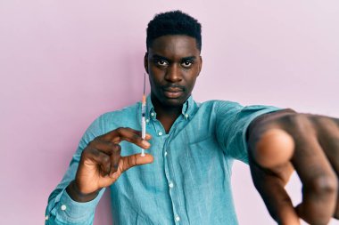 Elinde şırıngayla kamerayı işaret eden yakışıklı siyah bir adam ve sen, kendine güvenen ciddi görünüyorsun. 