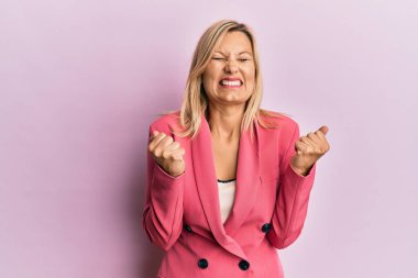 Orta yaşlı beyaz bir kadın iş ceketi giyiyor. Kolları havada ve gözleri kapalı zaferi kutluyor. Kazanan konsept. 