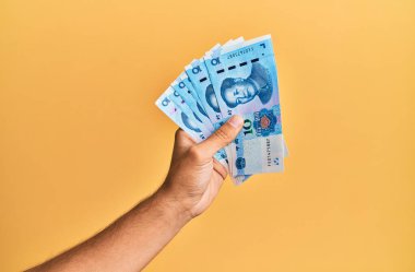 Çin malı 10 Yuan 'lık banknotları izole edilmiş sarı arka planda tutan İspanyol adamın eli..