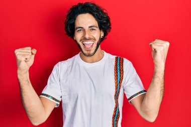 Yakışıklı, beyaz tişört giyen, gururla bağıran, zaferi ve başarıyı kutlayan kollarını kaldırarak heyecanlanan İspanyol bir adam. 